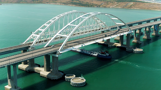 Top view of big bridge over green river. Action. Big white bridge with highway and traveling cars. Beautiful turquoise river with highway on bridge.