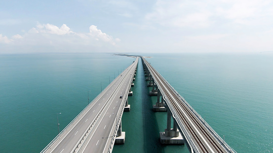 Aerial view along the long beautiful bridge above turquoise sea. Action. Flying above bending bridge with driving cars