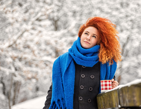 Beautiful young woman drinking hot cocoa outdoors during holidays