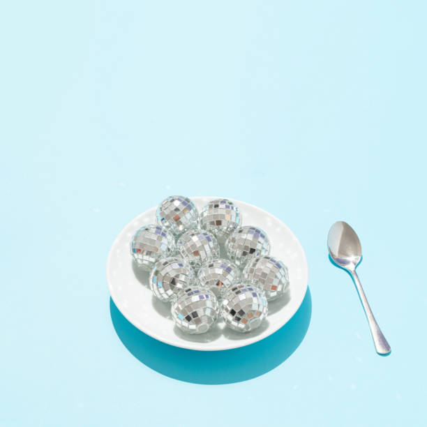 Disco balls in white plate and silver spoon on bright blue background. Minimal retro food party concept. Surreal festive artistic idea. New Year celebration aesthetic.