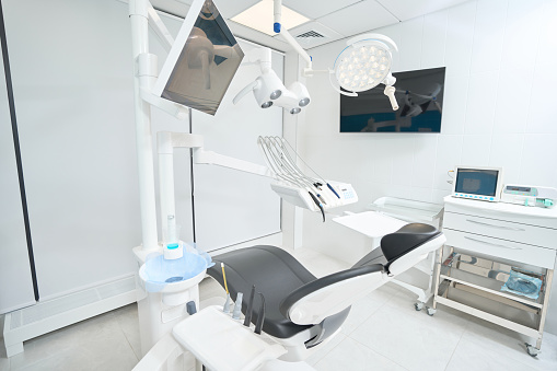Empty leather chair for stomatological patient with overhead light in dentist office