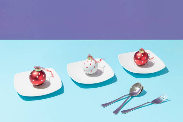 Three Christmas polka dots baubles on white plates and spoons and fork against bright blue and purple background. Minimal Christmas or New Year celebration concept. Creative holidays table composition.