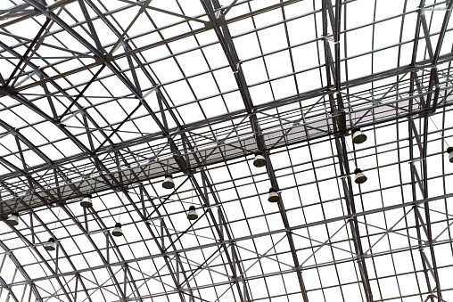 Metal geometric structure supporting a glass transparent roof. The architecture of a ceiling modern building with lamp lights and natural lighting
