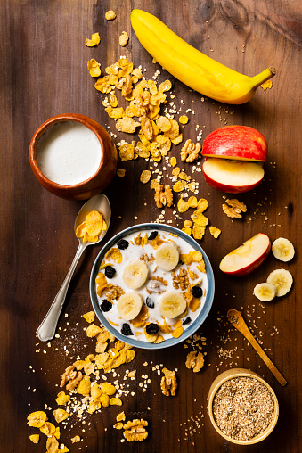 High angle view of healthy breakfast prepared at home . In the image are healthy organic ingredients as walnuts, apple fruit, banana, raisin, milk oats flakes and sesame in a small ceramic bowl over rustic wood table in the kitchen.Image was made with a full frame 24 megapixels camera with 35 mm f/stop 2.4 lens.