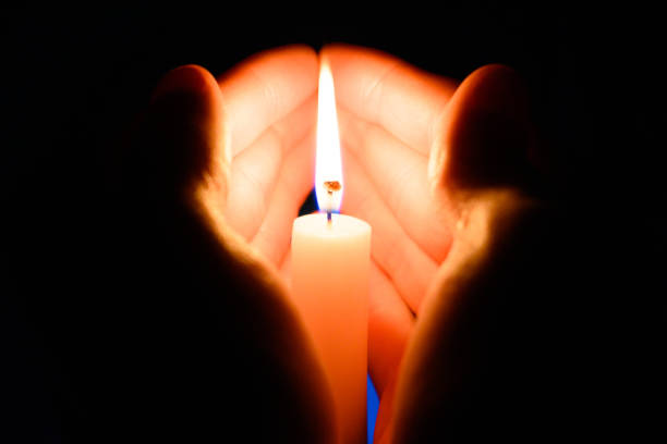 istock burning wax candle in the palms in the dark on a black background 1445854906