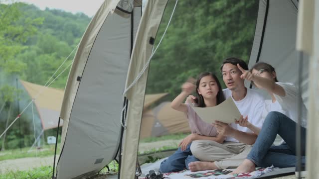 Two teenage girls and their father are looking at a secret map in a tent.