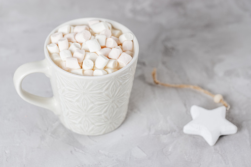 Cup of cocoa or chocolate with marshmallows and star Christmas decoration, light gray background. Winter hot beverage concept Flat lay, top view, copy space