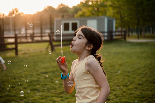 Portrait of a cute little girl blowing bubbles and playing at the park