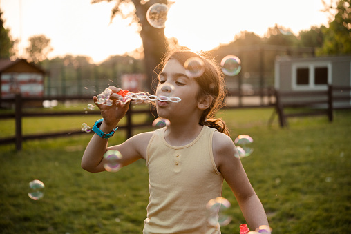 Portrait of a cute little girl blowing bubbles and playing at the park