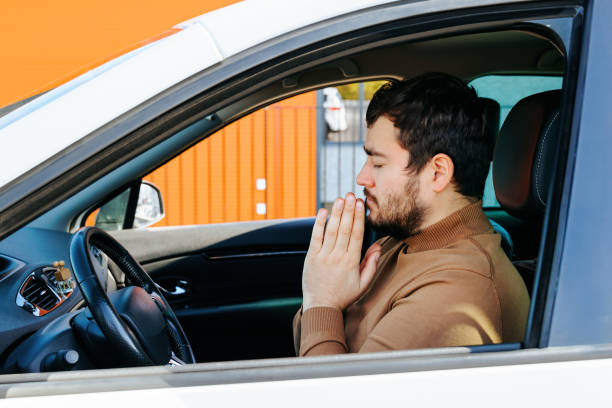 istock A young man sits in a car with his eyes closed, hands folded and praying. 1445857859