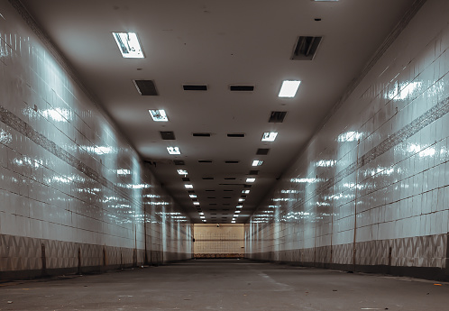 Bangkok, Thailand - Sep 30, 2022 : Perspective view of Ambient public underpass with white tiled walls and stripes of ceiling neon lights. Long pedestrian luminous tunnel, Space for text, Selective focus.
