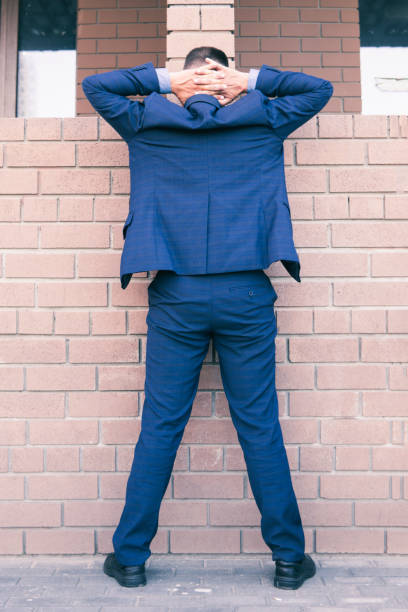 arrested man in a business suit stands against a brick wall with his hands raised up. Arrest and search of a corrupt deputy. Businessman under suspicion concept the arrested man in a business suit stands against a brick wall with his hands raised up. Arrest and search of a corrupt deputy. Businessman under suspicion concept terrorist financing stock pictures, royalty-free photos & images