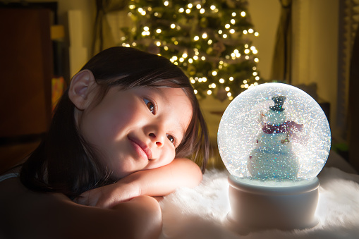 Child stares at snow globe with Christmas tree in background.