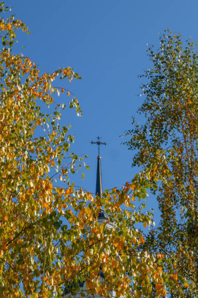 The cross of a Christian church against a blue sky surrounded by yellow autumn foliage of trees stock photo