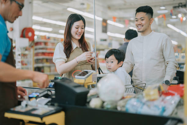 giovane famiglia cinese asiatica con il figlio check out alla cassa del supermercato che acquista prodotti lattiero-caseari e verdure - human pregnancy clothing shopping retail foto e immagini stock