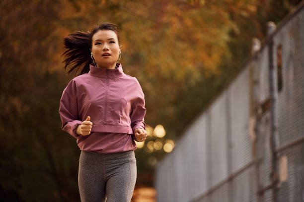 istock Young Asian athletic woman jogging through the park. 1445869421