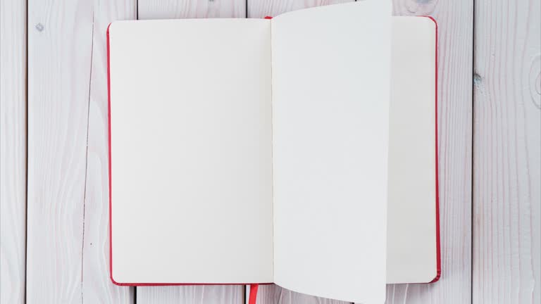 Red diary book with white empty papers, turning endless from right to left on white wooden background. Turn the page