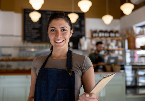 Happy woman working as a waitress at a cafe and looking at the camera smiling - food service concepts