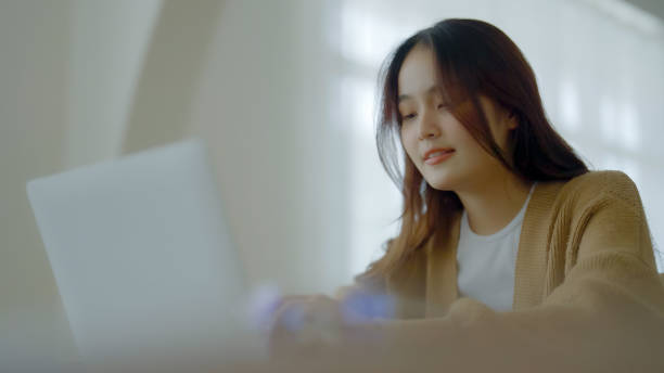 istock Smiling asian young woman working on laptop at home office. Young asian student using computer remote studying, virtual training, e-learning, watching online education webinar at house 1445891237