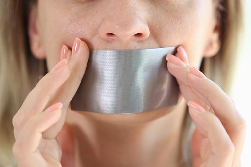 Close-up of young woman with duct tape sealed on mouth. Restriction of freedom of speech and censored or forbidden to speak and express opinion