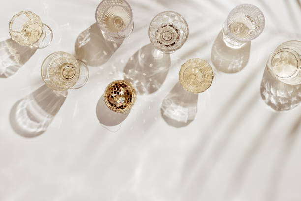 summer party flat lay, set crystal glasses with drink or champagne, mirror ball, white sparkling wine, beige golden aesthetic layout, holiday event concept, sunshine shadow from palm leaf - nobody alcohol champagne wine imagens e fotografias de stock