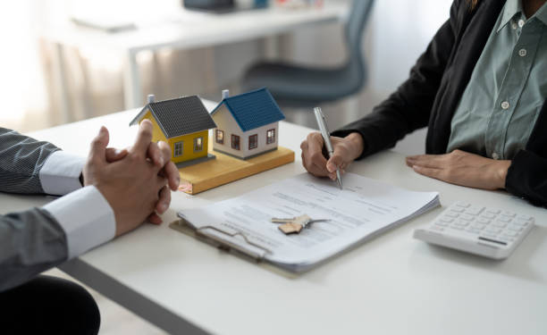 istock Real estate agent assisting client to sign contract at desk with house model 1445899059