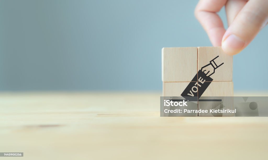Election vote concept. Hand putting paper in the voting box symbol on wooden cube blocks. Political election campaign logo. Applicable as part of badge design. Voting and polling symbols design. Accuracy Stock Photo