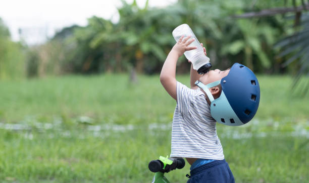 un mignon petit garçon sur un vélo portant un casque boit de l’eau d’une bouteille d’eau - water child bottle little boys photos et images de collection