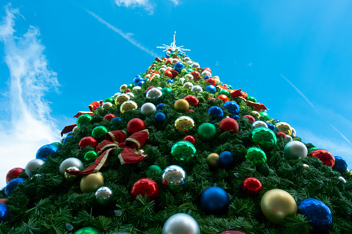 Close-up view of beautiful, decorated artificial Christmas tree with ornaments and a blue sky from below