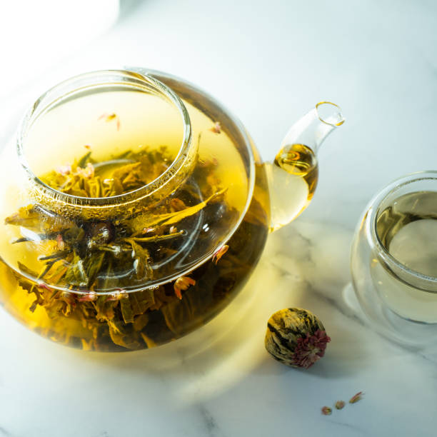 istock Chinese blooming tea. A glass teapot with a blooming tea flower on a white table. 1445904721