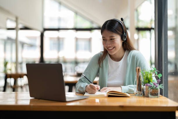 istock Young asian woman writing making list taking notes in notepad working or learning on laptop indoors- educational course or training, seminar, education online concept 1445907338