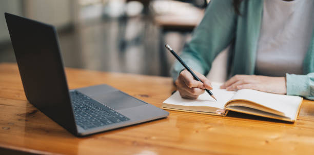 istock Cropped photo of woman writing making list taking notes in notepad working or learning on laptop indoors- educational course or training, seminar, education online concept 1445907346