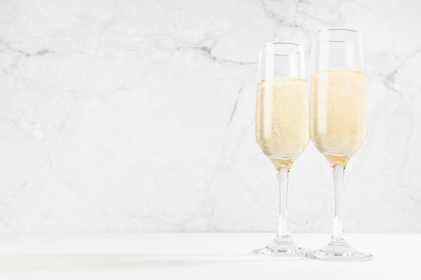 istock Festive background with sparkling champagne in  two glasses in white soft light interior on wood table and marble wall. Holiday drink for celebration event in restaurant, copy space. 1445910721
