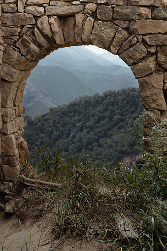 Ruin of old stone arch in medieval town on peak of in Caucasian mountains in Dagestan as frame with view on landscape with green slopes mountains in canyon. Archeology adventure and tourist trip.