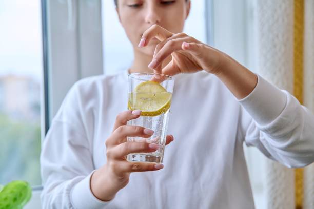 Close-up of glass of water with lemon in hands of young female stock photo