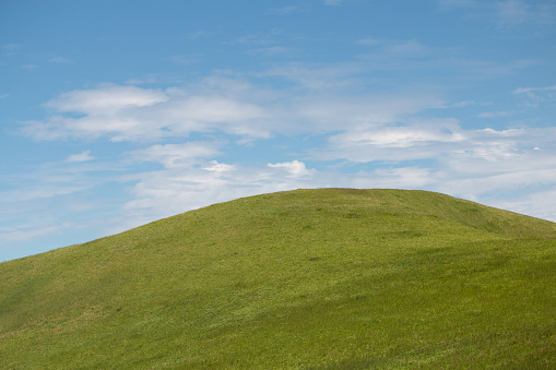 A plain green hill with blue sky and clouds in background