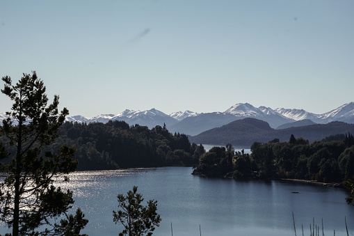 A scenic view of a lake against forests and mountains covered with snow in San Carlos de Bariloche, Argentina