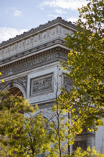 A vertical of Triumphal Arch of the Star depicted behind the yellow leaves in Paris, France