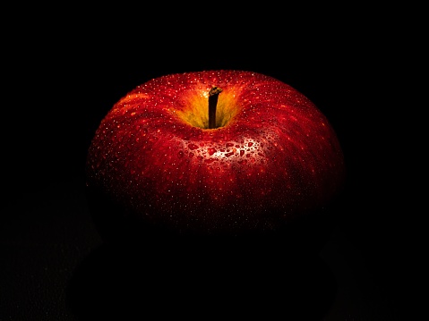 A red apple with waterdrops on it in shadow against black background
