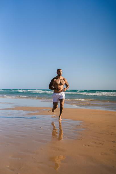 istock An attractive topless man with tattoos running on a beach next to a sea 1445919937