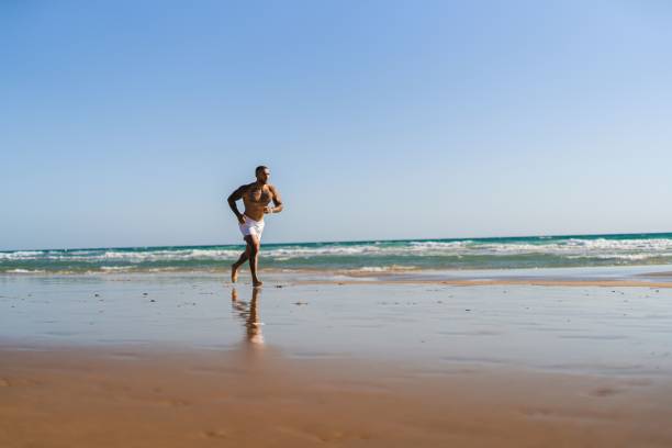 istock Attractive topless man with tattoos running on a beach next to a sea 1445919956