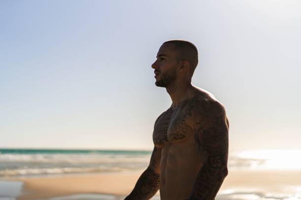 istock An attractive topless man with tattoos standing  on a beach next to a sea 1445920137