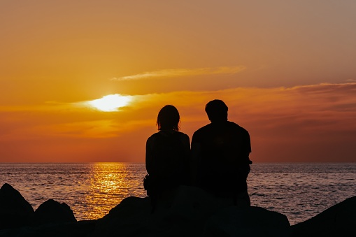 The silhouettes of a couple enjoying sunset over the ocean sitting on the rock