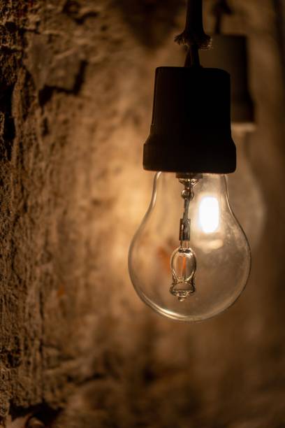 istock Vertical closeup shot of a bare light bulb hang on an old wall 1445923737