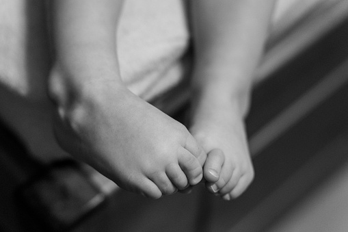 A grayscale shot of a child's legs play with each other