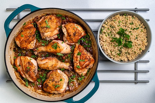 A top view of Umbrian-Style Chicken alla Cacciatora in a pan near a bowl of couscous with greens