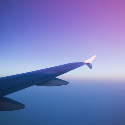 A scenic view of a plane wing from the window with a breathtaking purple sunset skyscape in the background