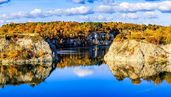A gorgeous landscape with a tranquil lake reflecting cliffs and vibrant autumnal trees under a cloudy sky