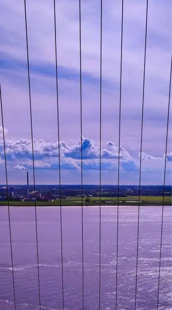 A vertical shot of a coastal city from a bridge with suspender cables with the sky illuminating purple