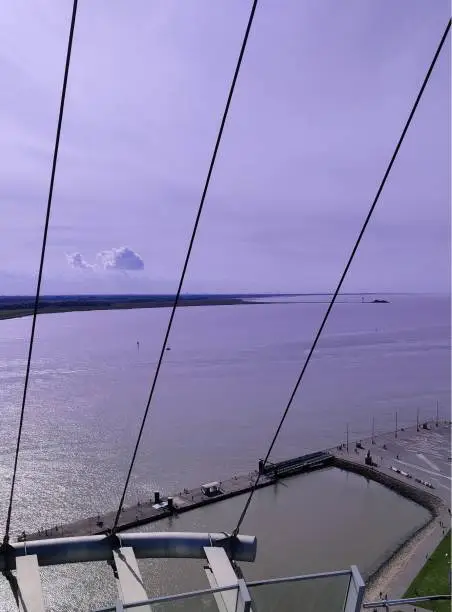 A vertical shot of the ocean from a bridge with suspender cables with the sky illuminating purple